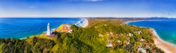 Top Of Headland With Byron Bay Lighthouse High Above Pacific Ocean Coast On A Sunny Day In Elevated Aerial Panorama Facing Inland Over Sandy Beaches.