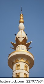 the top of the minaret of a mosque painted in white, yellow and gold decorated with a bright blue sky - Shutterstock ID 2279776347