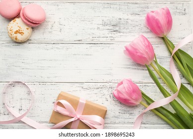 Top overhead close up flat lay photo of delicate tulips silky ribbon and yummy tasty delicious macaroons on wooden white table - Powered by Shutterstock