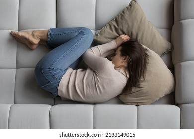 Top overhead view young peaceful woman lying on sofa at home. Female feels sick, suffers from illness or depression, thinking about personal problems, looking lonely. Daytime nap, life concern concept