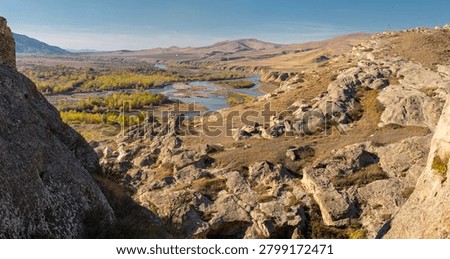 Top panoramic view of winding river Kura against grassy slopes in Caucasus mountains in Georgia at sunny autumn day. Mountain valley beautiful scenery. Rocks and cliffs in the foreground