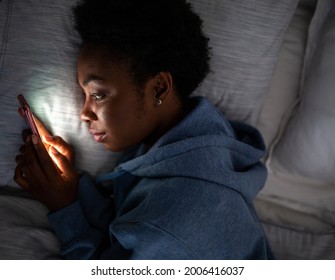 Top portrait young African American woman looking at cellphone in bed - Powered by Shutterstock