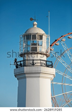 Top of a pristine white lighthouse stands beside a colorful ferris wheel in Batumi, Georgia