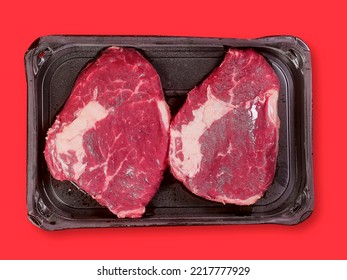 Top quality rib eye steak on a black plastic tray and red color surface background. Premium meat cut product. Butcher craft. Food supply industry. - Powered by Shutterstock