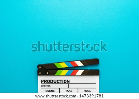 Top section of white clapperboard at the bottom of turquoise blue background with copy space. Top view photo of open movie clapboard as filmmaking concept. Minimalist flat lay of film slate.