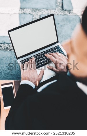 Top selective view on skilled male manager of financial website sitting outdoors with laptop computer with blank screen area for internet advertising and looking away while updating antivirus