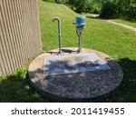 The top of a sewer lift located in Nova Scotia. There are two pipes. One is curved and looks like a cane. The other is capped with a light blue top. The cover is cement and round with a door hatch.