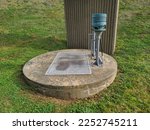 The top of a sewer lift located in Nova Scotia. There are two pipes. One is curved and looks like a cane. The other is capped with a light blue top. The cover is cement and round with a door hatch.