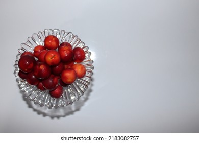 Top shot of luscious red plums on a glass serving platter on a white table and in front of a white background