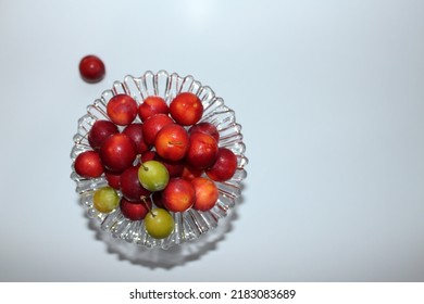 Top shot of luscious red plums and green plums on a glass serving platter on a white table and in front of a white background