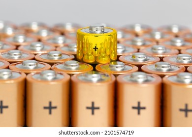 Top side view of the positive terminals of 1.5 V AA Alkaline batteries. A yellow-coated battery in selective focus has reflections from other batteries. Differences concept.