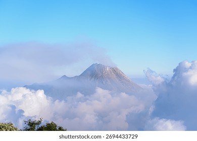 Top summit of Mount Merapi, the most active volcano in the world, emit toxic gas and ashes from magma lava crater. In morning or afternoon, it is surrounded with cloud, fog, and mist with blue sky 