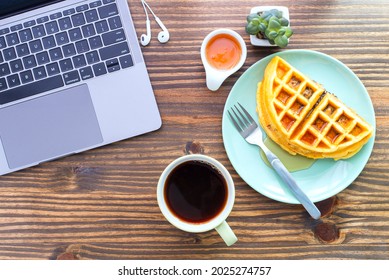 Top table view flat lay on a desk with a laptop computer, cup of coffee and Waffle on green plate with honey cup and cell phone earbuds. Concept of morning working with easy breakfast, ready to work. - Powered by Shutterstock