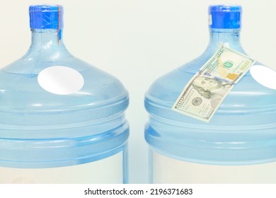 The Top Of Two Plastic Gallon Water Bottle Containers With White Round Labels And 100 Dollars Stand On A White Background. Refreshment. Retail. Water. Refresh. Cooling. Stand. Cold. Delivering