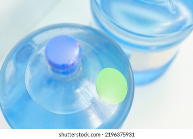 The Top Of Two Plastic Gallon Water Bottle Containers With Green Round Labels Stand On A Blue Background. Healthy. Object. Transparent. Clear. Bottled. Cooler. Freshness. Mineral