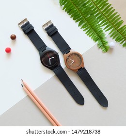 Top view of 2 black wooden watches on white and brown color background. Green leafs,pencil and leather band watch on soft color background. - Powered by Shutterstock