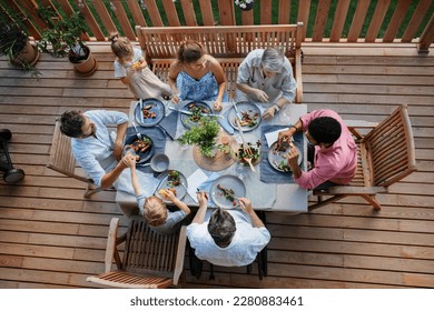 Top view of 3 generations family eating at barbecue party dinner on patio, people sitting at table on patio with grill. - Powered by Shutterstock