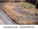 Top view of an abandoned empty lot in a town, with dry grass surrounded with metal wire mesh fencing, sunny day. Empty city lot available for development. Empty property in a city. Land for sale