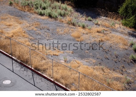 Top view of an abandoned empty lot in a town, with dry grass surrounded with metal wire mesh fencing, sunny day. Empty city lot available for development. Empty property in a city. Land for sale