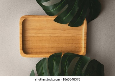 Top View Above Empty Bamboo Wooden Square Plate Decoration Setting With Artificial Monstera Deliciosa Or Swiss Cheese Plant Dark Green Leaves On Grey Organic Paper Background.