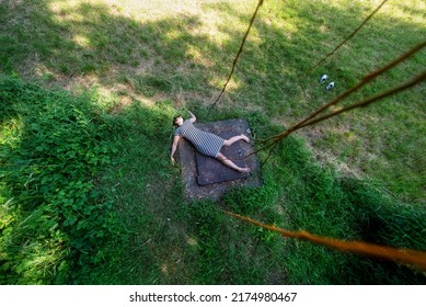top view from above of sexy young brunette woman, lying dead in black and white striped tight dress on square metal lid cover in rural grass meadow, copy space