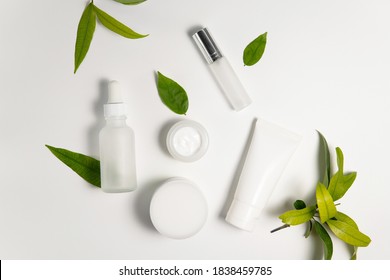 Top view above various set organic facial skincare product white tube, serum, spray bottle, cream lotion container decoration with branch of plant and green leaves on plain white isolated background