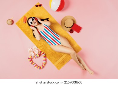 Top view from above young woman of Asian ethnicity in striped swimsuit headphones listen music lies on towel hotel pool isolated on plain pastel pink background Summer vacation sea rest suntan concept - Powered by Shutterstock