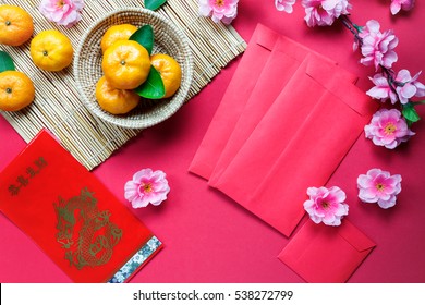 Top view accessories Chinese new year festival decorations.orange,leaf,wood basket,red packet,plum blossom on red background.Foreign language means be rich and Happy.
