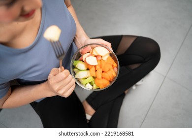 Top View Of Active Woman Sitting And Eating Cut Red And Green Apple Mixed With Carrot In Glass Bowl Picking With A Fork. A Dieting Vegetarian Meal.