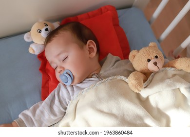 Top View Of Adorable Baby Boy Sleeping With Pacifier On Mouth In Cot With Teddy Bear Toy. Mixed Race Asian-German Infant Lying In Crib. Little Child Sleep With Blanket.