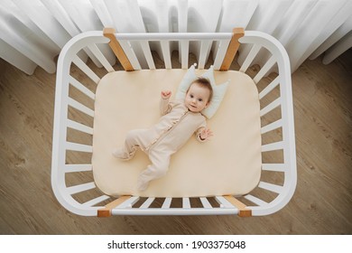 Top view of adorable infant in stylish pajama lying on pillow crown in comfortable cot at home. Baby in cradle