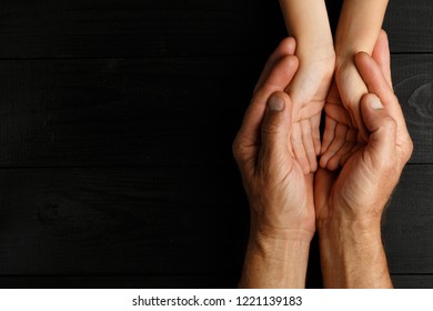 Vista superior, Manos adultas sosteniendo manos de niños, Concepto de Ayuda Familiar, manos pequeñas en la mano de los padres. sobre fondo de madera negra