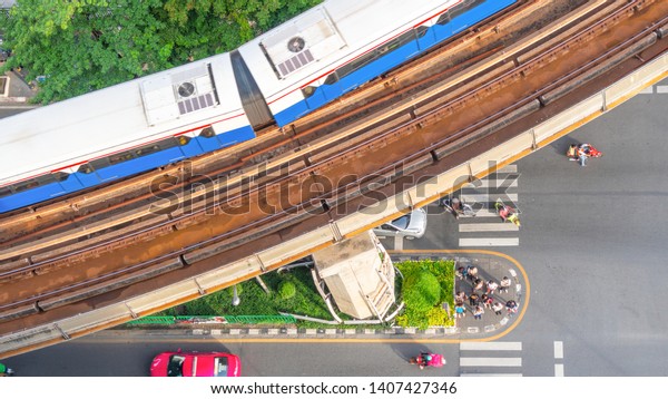 Top view aerial of a driving car on asphalt track\
and pedestrian crosswalk in traffic road  with sky train run on the\
top rail.