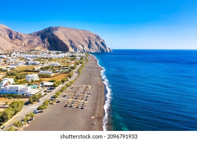 Top View Aerial Drone Photo Of Black Perissa Beach With Beautiful Turquoise Water, Sea Waves And Straw Umbrellas. Vacation Travel Background. Aegean Sea, Santorini Island, Greece.