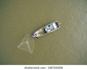 Top View, Aerial View, Of Fisher Man On Old Wooden Boat Fishing By Throwing Fishing Net To River.