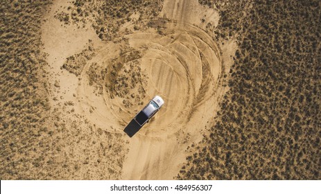Top view aerial photo from drone of a riding pickup machine in sandy steppe during amazing trip to Asia. Professional rider is drifting in desert arid wilderness while leaving trails of the tires