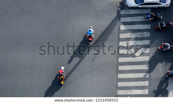 Top view\
aerial photo of motorcycle driving pass pedestrian crosswalk in\
traffic road with light and shadow\
silhouette