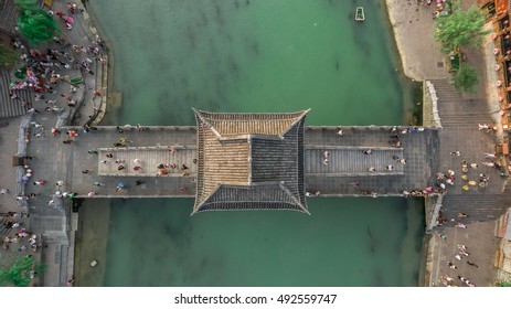 Top View Or Aerial Shot Of Famous Stone Old Fashioned Chinese Bridge In  Ancient Town In Fenghuang County, China. Aerial View Of Stone Bridge Over Green River, Crowds Of People.   