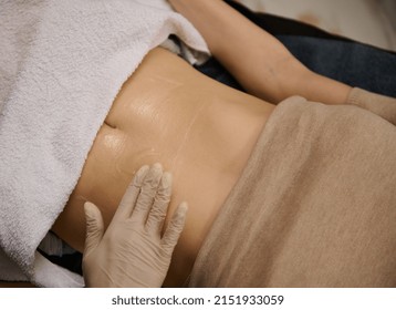 Top view of aesthetician hands applying contact gel on the belly of woman lying on a daybed in wellness spa clinic, before receiving medical treatment
