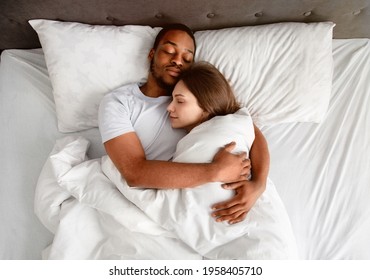 Top view of affectionate multiracial couple hugging each other while sleeping in bed. Overhead shot of loving young family cuddling next to each other, embracing in their sleep
