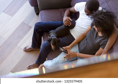 Top View African American Couple Sitting With Sleeping Dog, Using Phone Together, Looking At Screen, Viewing Photo In Social Network, Browsing Mobile Apps, Black Man Embracing Attractive Woman