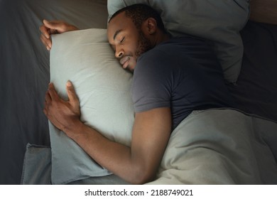 Top View Of African American Man Sleeping Embracing Pillow Lying In Bed In Modern Bedroom Indoor. Millennial Guy Napping Resting At Home. Healthy Sleep Concept - Powered by Shutterstock