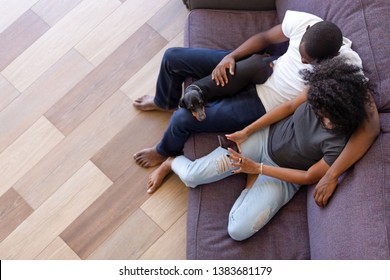 Top View Of African American Young Family With Dog Sit On Couch Relaxing Using Smartphone Shopping Online, Black Couple Rest On Sofa At Home With Pet, Browsing Cellphone Or Showing Pictures On Cell