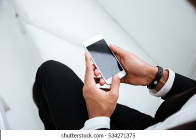 Top View Of African Business Man In Black Suit Holding Phone In Hands In Office. Cropped Image