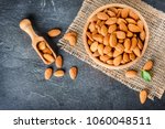 Top view of almonds on dark stone table with wood spoon or scoop. Almond in wooden bowl. Nuts freely laid on dark board.