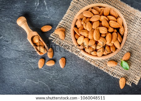 Top view of almonds on dark stone table with wood spoon or scoop. Almond in wooden bowl. Nuts freely laid on dark board.