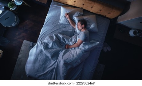 Top View Apartment Bedroom: Handsome Young Man Sleeping Cozily on a Bed in His Bedroom at Night. Comfortable Apartment with Guy Resting for Productive next Day. Top Down Above - Powered by Shutterstock