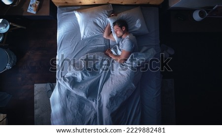 Top View Apartment Bedroom: Handsome Young Man Sleeping Cozily on a Bed in His Bedroom at Night. Comfortable Apartment with Guy Resting for Productive next Day. Top Down Above