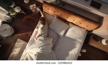 Top View Apartment: Handsome Young Man Sleeps in His Bed, Turns off Alarm Clock on Smartphone, Greets New Sunny Day. Joyful Waking Up of a Guy who is Ready for Productive Day. Top Down Shot - Powered by Shutterstock