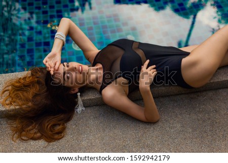 Top view of appealing seductive model in black swimwear relaxing  near pool. Perfect brunette hairs and skin.